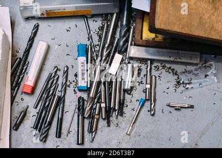 Top view of various metal twist drill bits and tools scattered on table in professional workshop Stock Photo
