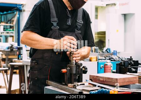Crop anonymous factory worker wearing uniform working on lathe with drilling machine in contemporary light craftsmanship Stock Photo