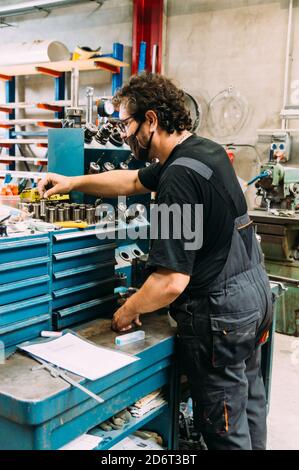 Side view busy adult male engineer wearing uniform and protective face mask working in modern equipped factory Stock Photo