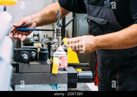Crop anonymous workman in uniform working on drilling machine in modern industrial manufacture Stock Photo