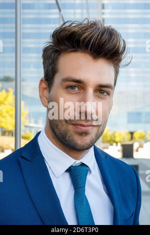 Handsome young stylish male entrepreneur in formal suit and tie standing on street on sunny day and looking at camera Stock Photo