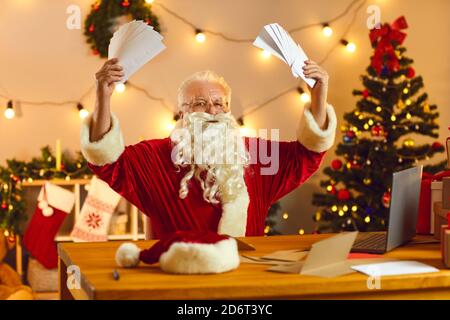 Amazed senior Santa Claus holds in his hands a lot of letters from children with wish lists. Stock Photo