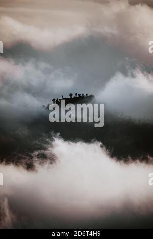 Dramatic scenery of dark mountain top seen through dense gray clouds and fog in highlands Stock Photo