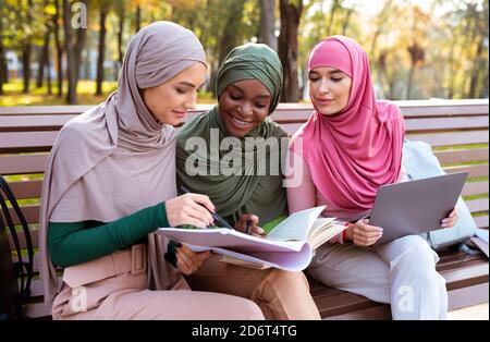 Three Muslim Students Women Learning Together Using Computer Sitting Outdoors Stock Photo