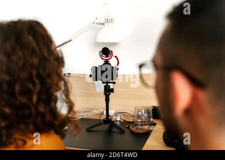 Back view of focused young couple blogger with curly hair in casual outfit and eyeglasses and professional photo camera placed on tripod while shootin Stock Photo