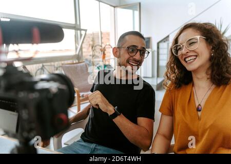 Side view of focused young couple blogger with curly hair in casual outfit and eyeglasses and professional photo camera placed on tripod while shootin Stock Photo