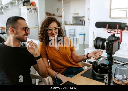 Side view of focused young couple blogger with curly hair in casual outfit and eyeglasses and professional photo camera placed on tripod while shootin Stock Photo
