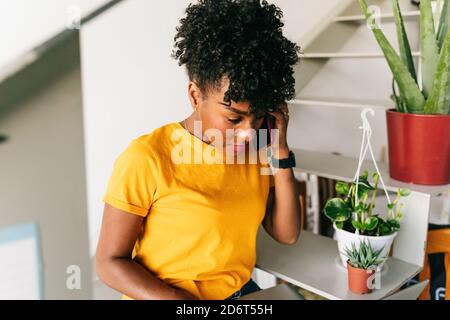 modern young black female freelancer with phone and browsing laptop while working on remote project at home Stock Photo