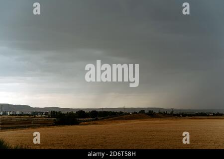 Vast agricultural fields in green countryside against dramatic overcast sky covered with dark heavy clouds Stock Photo