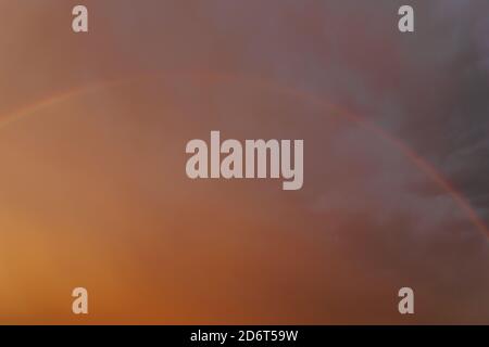Scenery of vibrant rainbow shining on dark dramatic sky covered with thick heavy clouds in evening Stock Photo
