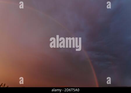 Scenery of vibrant rainbow shining on dark dramatic sky covered with thick heavy clouds in evening Stock Photo