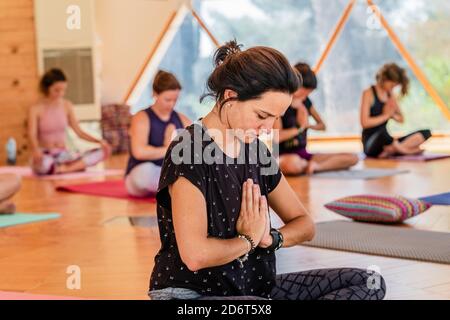 Group of female in sportswear sitting with crossed legs and closed eyes while practicing yoga on mats in room Stock Photo