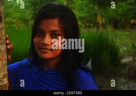 Close up of a teenager girl holding a tree and smiling in a paddy field of West Bengal in India, selective focusing Stock Photo