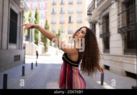Young fit ethnic female dancer with long curly hair dancing on paved street looking away Stock Photo