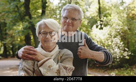 Happy old couple hugging in park. Senior man flirting with elderly woman. Thumbs up. High quality photo Stock Photo
