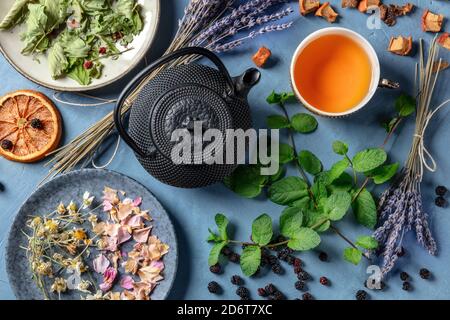 Herbal tea, natural, organic, and healthy, a tea pot, cup, and a variety of ingredients, shot from above on a blue background Stock Photo