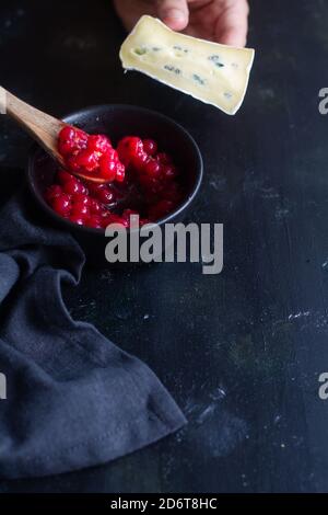 From above crop unrecognizable person putting mashed red currants on slice of fresh Gorgonzola cheese above black table surface Stock Photo
