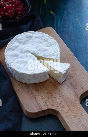 From above composition of soft Camembert cheese truckle placed on wooden cutting board near bowl with currant Stock Photo