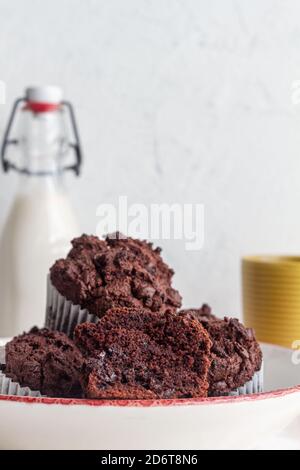 High angle tasty sweet chocolate cupcakes heaped on plate near jar with fresh milk in light kitchen Stock Photo