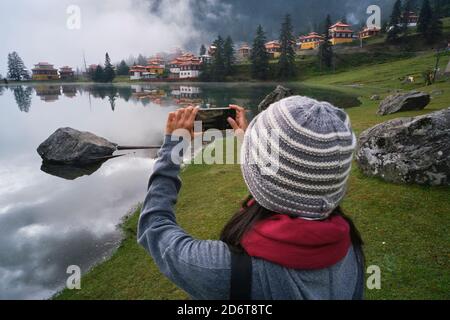 High angle back view of unrecognizable female tourist shooting calm lake located in highland area near Buddhist temple Stock Photo