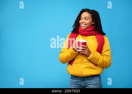 Black Lady In Jacket Holding Cup Looking Aside, Blue Background Stock Photo