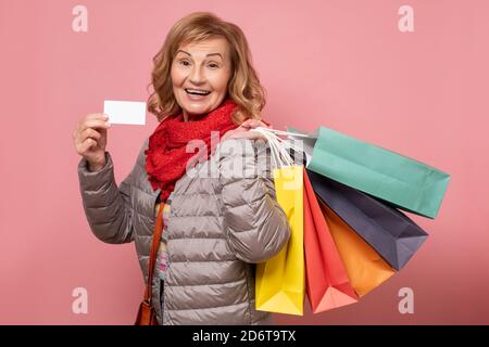 Mature happy smiling woman with shopping bags, isolated over pink background Stock Photo