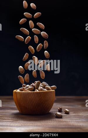 Pistachios in a wooden Cup on a dark background. Flying food. Space for text Stock Photo
