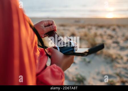 From above of crop anonymous female traveler setting vintage film camera while standing on sandy beach at sunset Stock Photo