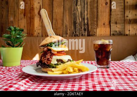 Appetizing burger with vegetables and cutlet on plate with French fries served on table with glass of cold coke in rustic cafe Stock Photo