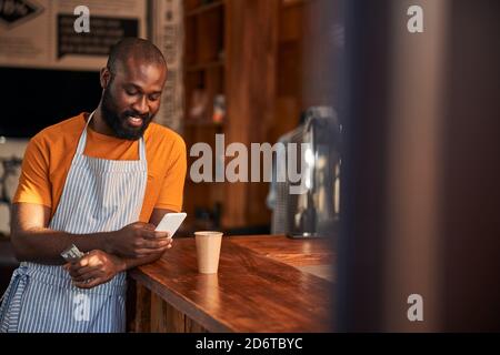 Cheerful Afro American man using cellphone in barbershop Stock Photo