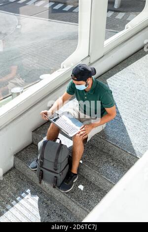 From above of male tourist sitting on stairs in airport and browsing netbook while waiting for departure Stock Photo