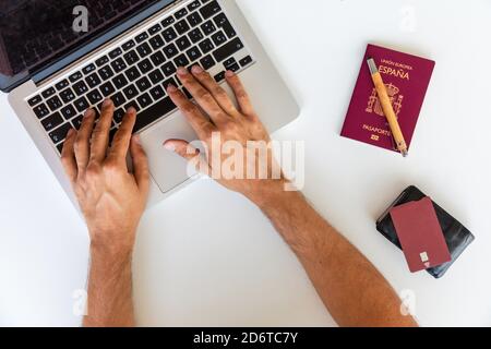 From above of male tourist typing on laptop while searching for air tickets for vacation while sitting at table with passport and plastic card Stock Photo