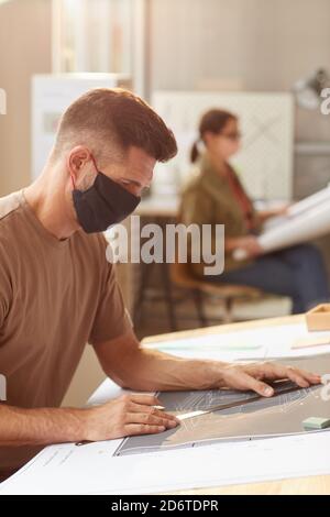 Side view portrait of mature bearded architect wearing mask while sitting at drawing desk in sunlight Stock Photo