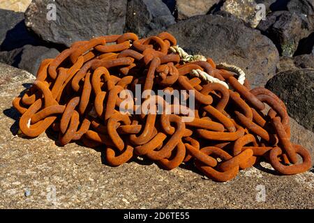 A piled up length of rusty chain glows in the afternoon sun on the concrete slipway by the marina in Ledaig at Tobermory Stock Photo