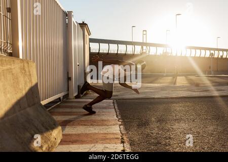 Full body side view of African American athlete wearing wireless headphones doing jogging exercises while training outdoors Stock Photo