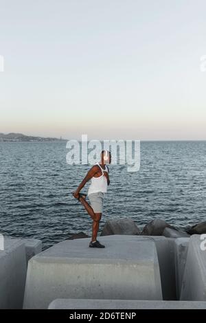 Full body side view of African American runner warming up before running while listening to music in wireless headphones Stock Photo