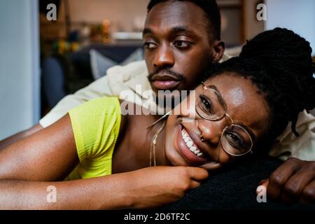 Happy young black man in casual clothes lying on back of girlfriend while spending weekend together at home Stock Photo