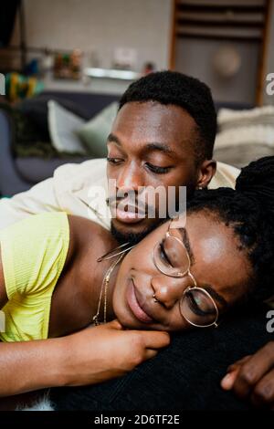 Happy young black man in casual clothes lying on back of girlfriend while spending weekend together at home Stock Photo