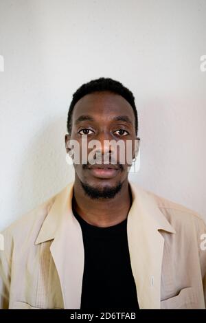 Pensive young African American male in light beige formal shirt thoughtfully looking away while standing near white wall Stock Photo