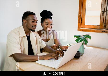 From above of positive young African American man and Woman in casual clothes and smiling while working together on laptops at home Stock Photo