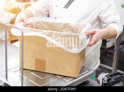 A worker in production weighs products in a box on scales, packing and sorting products by weight, industry, workman Stock Photo