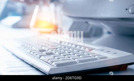Computer keyboard and test tube with orange liquid in the laboratory. The concept of conducting experiments in chemistry and medicine, professional Stock Photo