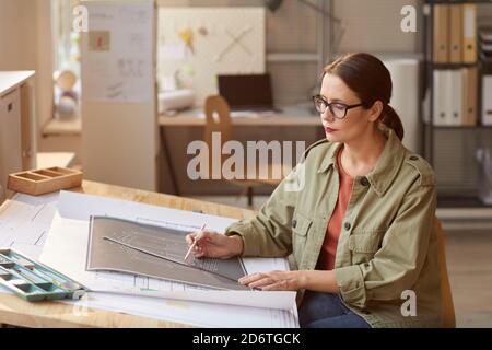 Portrait of young woman drawing blueprints and plans while working at desk in engineers office, copy space Stock Photo