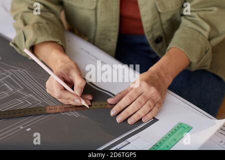 Close up of young woman drawing blueprints and plans while working at desk in engineers office Stock Photo