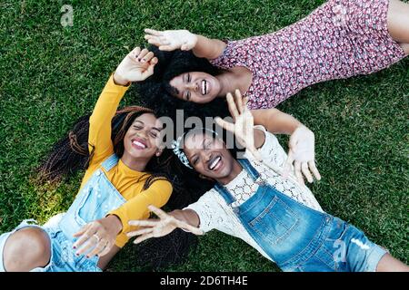 High angle of happy multiracial girlfriends lying together on grass and stacking hands while resting in park in summer Stock Photo