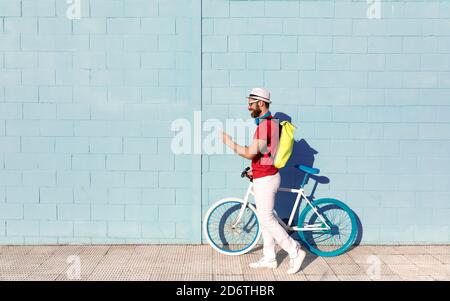 Side view of unrecognizable young guy in casual outfit using mobile phone while standing near stylish bicycle and blue wall on city street Stock Photo