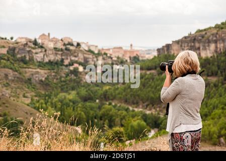 Side view of unrecognizable mature female photographer with professional photo camera taking pictures of old town Cuenca with medieval buildings on hi Stock Photo