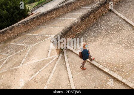 From above side view of female traveler with backpack and protective mask walking up paved stairway while sightseeing in medieval Cuenca town in Spain Stock Photo