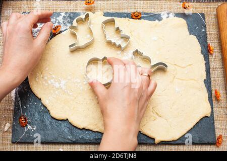 Making cookies for Halloween. A woman cuts out cookies from the dough in the form of pumpkin, cat, Ghost and bat. Stock Photo