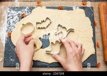 Making cookies for Halloween. A woman cuts out cookies from the dough in the form of pumpkin, cat, Ghost and bat. Stock Photo